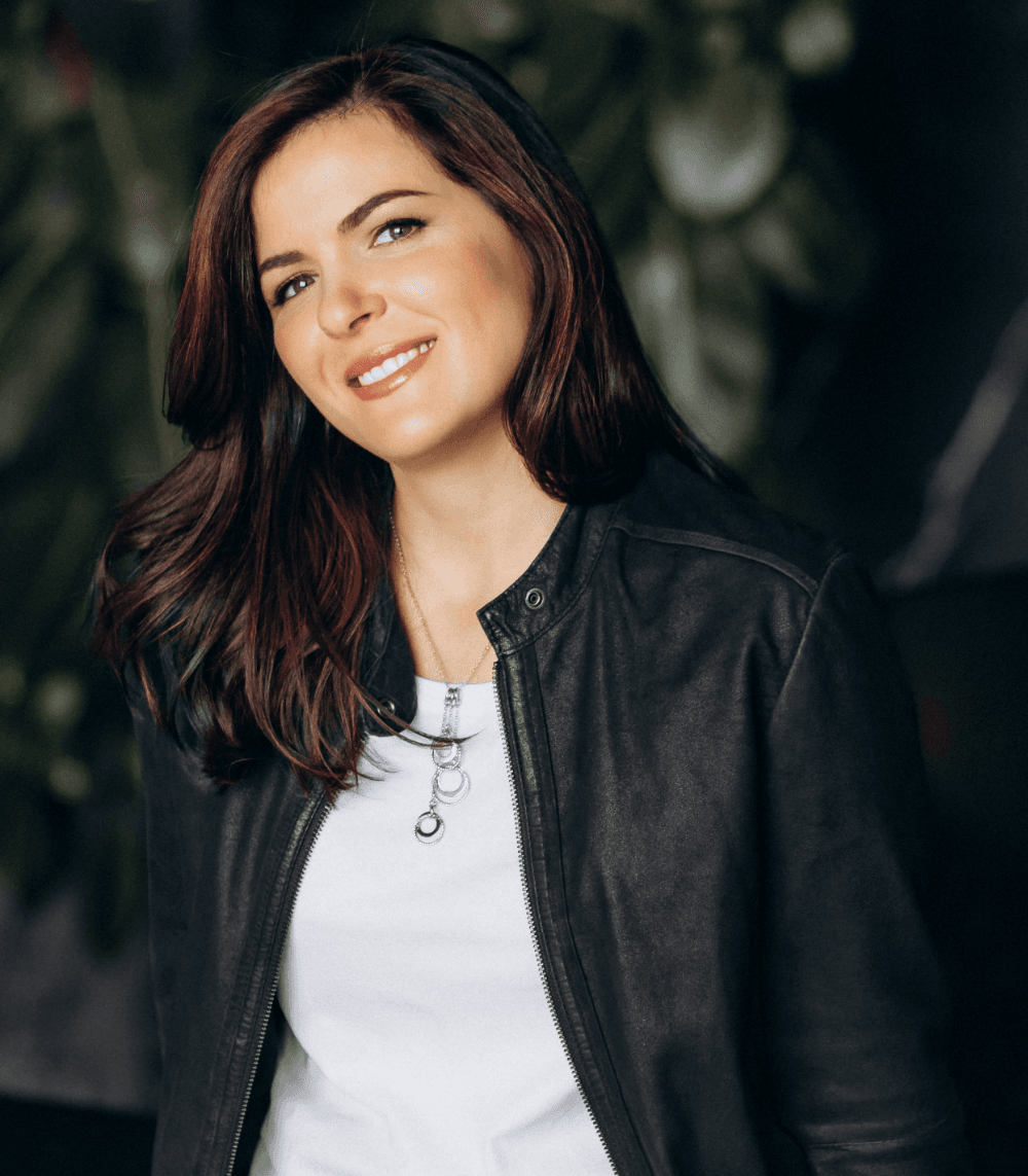Smiling Anna Sher wearing a black leather jacket and white shirt